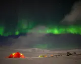 Nocne niebo rozświetla zorza polarna, a pod nią rozbijają się namioty. Idealny moment na obserwację tego zjawiska.