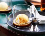 Ein cremiger Affogato mit Alkohol, serviert in einem Glas mit einer Kugel Vanilleeis, übergossen mit Espresso und einem kleinen Schnapsglas daneben.