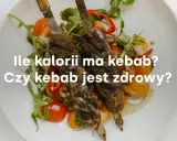 Dwa szaszłyki z mięsem i warzywami na talerzu. Tekst pyta: "Ile kalorii ma kebab? Czy kebab jest zdrowy?".