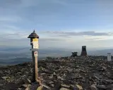 Szczyt Babiej Góry. Znaki wskazują, ile się wchodzi na Babią Górę, a w oddali rozciąga się malowniczy krajobraz.