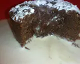 Un fondant au chocolat dégoulinant, saupoudré de sucre glace, servi dans une sauce crémeuse sur une assiette rouge.