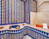 Ein luxuriöser Hamam in Marokko, verziert mit blauen und orangen Zellige-Fliesen. Kerzen und Schalen mit Rosenblättern schaffen eine entspannende Atmosphäre.