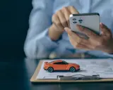Pomarańczowy mini **casco** na dokumentach, obok dłoni trzymającej smartfon.