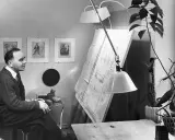 Paavo Tynell sitter vid sitt ritbord, omgiven av sina skisser och en stor ritning.