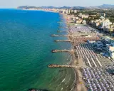 Vista aerea della costa adriatica, con la spiaggia affollata di ombrelloni e stabilimenti balneari, che si estende fino a Cattolica e Misano.