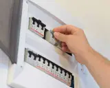 Main disjoncteur général manipulé par une main dans un tableau électrique blanc.