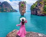 Donna con abito rosa e cappello bianco ammira la spettacolare **isola di James Bond** con le sue formazioni rocciose uniche e il mare turchese.