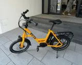 Gelbes i:SY E-Bike, das bei der Stiftung Warentest gut abgeschnitten hat, steht auf gepflastertem Untergrund vor einer Treppe.