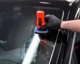 Rękawiczka z czarną rękawiczką nakłada preparat na szybę. To pokazuje, jak działa powłoka hydrofobowa, co to znaczy, że woda spływa.