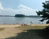 Słoneczny dzień nad jeziorem przeczyckim. Ludzie odpoczywają na piaszczystej plaży, kąpią się i pływają.