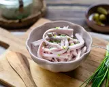 Schmackhaftes Fleischsalat Rezept mit Gurkenstückchen und Schnittlauch garniert, serviert in einer Schale auf einem Holzbrett.