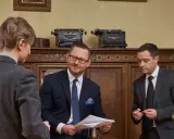 Czterech mężczyzn w garniturach rozmawia w gabinecie z zabytkowymi maszynami do pisania.