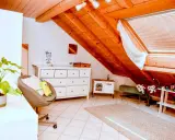 Acogedor despacho en buhardilla con vigas de madera, cómoda blanca, sillón y alfombra.