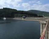 Betonowa zapora spiętrza wody Jeziora Żywieckiego. W oddali zielone wzgórza i błękitne niebo z chmurami.