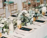 Elegancko nakryty stół z menu i kwiatami. Złote krzesła i zielone kieliszki tworzą atmosferę uroczystego obiadu weselnego zamiast wesela.