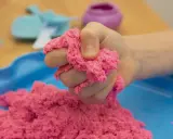 Kind hält pinken kinetischen Sand, der sich leicht formen lässt. Perfekt zum **kinetic sand selber machen** und Spielen.