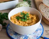 Pyszna pasta z kurczaka w miseczce, udekorowana natką pietruszki, obok czosnek i kromki chleba.