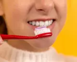 Uśmiechnięta twarz z białymi zębami, na czerwonej szczoteczce pasta do zębów. Dbanie o higienę to podstawa, jak lakierowanie zębów.