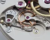 Meccanismo di orologio con ingranaggi dorati e ruota bilanciere, parte di uno scappamento coassiale.