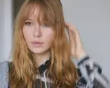 Ein junges Mädchen mit langen, welligen Haaren und Pony, das sich die Haare stylt.
