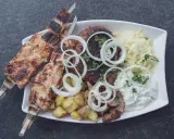 Ein Teller mit gegrilltem Fleisch, Kartoffeln und Krautsalat, garniert mit Zwiebelringen. Ein authentisches Souvlaki Rezept original.