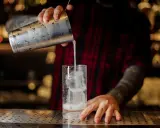 Barkeeper gießt einen erfrischenden Gin Fizz mit Eis in ein Glas.