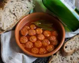 Chorizo a la sidra en cazuela de barro, acompañado de pan rústico y una botella de sidra verde.