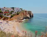 Sonnige Küste Portugals mit weißem Strand, türkisfarbenem Meer und Häusern auf den Klippen. Perfekt für eine Portugal Wetter Jahresübersicht.