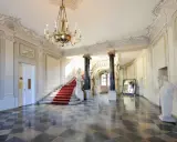 Elegancka klatka schodowa z czerwonym dywanem i żyrandolem w Pałacu Branickich w Białymstoku. Sprawdź cennik zwiedzania!