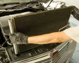 Mechanik w rękawicach wyjmuje skraplacz klimatyzacji z samochodu.