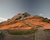 Szlak na Giewont z dzieckiem. Kamienna ścieżka wije się po zboczu oświetlonym słońcem, prowadząc ku szczytowi z krzyżem.