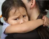 Ein Kind weint im Kindergarten und klammert sich an seine Mutter. Die Kleine hat Tränen in den Augen und sucht Trost.
