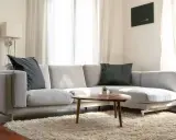 Un cómodo cheslón gris con cojines oscuros, alfombra mullida y mesa de centro de madera.