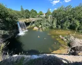 Gente disfrutando de un día soleado en las pozas del río Tus, con una cascada y vegetación exuberante.