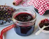 Frisch zubereitete holunderbeeren marmelade im Glas, daneben frische Beeren und eine kleine Schale mit Löffel.