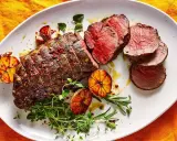 Roast beef al horno jugoso y tierno, servido con ajos asados y hierbas frescas.