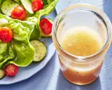 En burk med hemlagad salladsdressing bredvid en fräsch sallad med gurka och tomater. Ett perfekt salladsdressing recept för en lätt lunch.