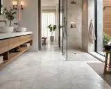 Bagno moderno con pavimenti e rivestimenti in **segato di marmo** bianco, doppio lavabo, doccia a vista e arredi in legno.