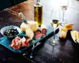 En härlig italiensk buffé med ost, salami, prosciutto, oliver, bröd och ett glas vitt vin, kanske en riesling druva.