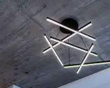 Oryginalna lampa sufitowa z geometrycznymi, podświetlanymi ramionami, zawieszona na tle surowego, betonowego stropu.