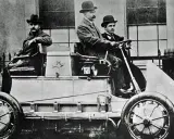 Hombres con sombreros posan en el primer coche eléctrico de la historia, un vehículo pionero de finales del siglo XIX.