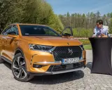 Pomarańczowy Citroën DS7 Crossback z otwartymi drzwiami, obok stolika z winem i bagietką, na tle zieleni.