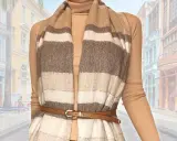 Modello che mostra come indossare una sciarpa grande a righe, abbinata a un dolcevita e una cintura sottile, con uno sfondo di edifici colorati.
