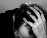 Uomo con mano tra i capelli, ombra scura sul volto. Potrebbe rappresentare il peso di una diagnosi di linfoma cutaneo.