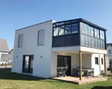 Maison moderne avec extension étage sur piloti. Une véranda vitrée surplombe une terrasse en bois.