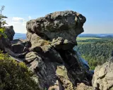 Wielkie, szare skały górują nad zieloną doliną. W oddali widać pola i lasy, a na niebie błękit i chmury.