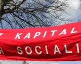 Röd banderoll med vit text: "MOT KAPITALIS FÖR SOCIALIS". En demonstration som visar vad socialism betyder.