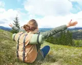Kobieta z plecakiem na cergowym szlaku, z ramionami otwartymi na oścież, cieszy się pięknem górskiego krajobrazu.