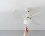 Mano tira de la cadena de un ventilador de techo pladur blanco, iluminando la habitación.