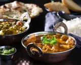 Delicioso pollo tikka masala cremoso, acompañado de arroz basmati, pan naan y una guarnición verde.
